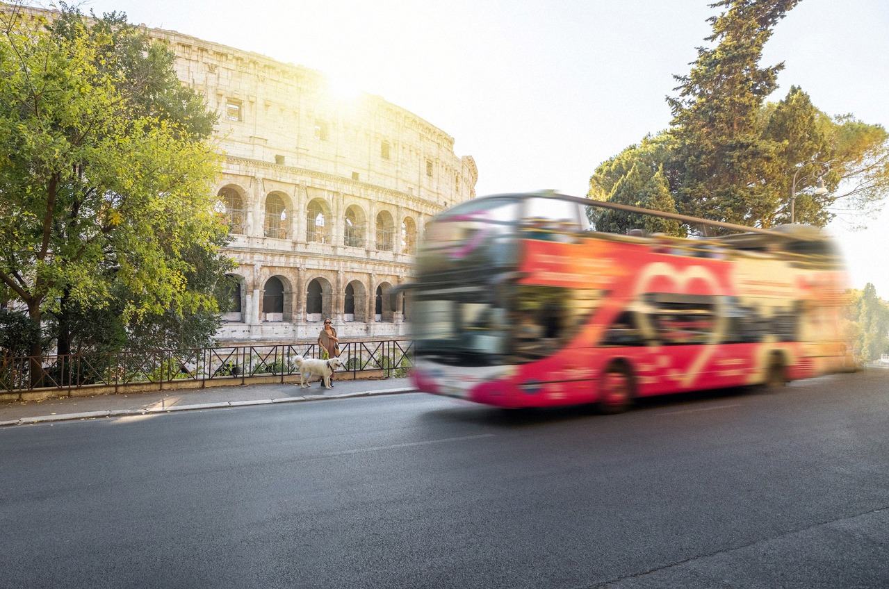 Red hop-on-hop-off double-decker bus passing the Colosseum in Rome