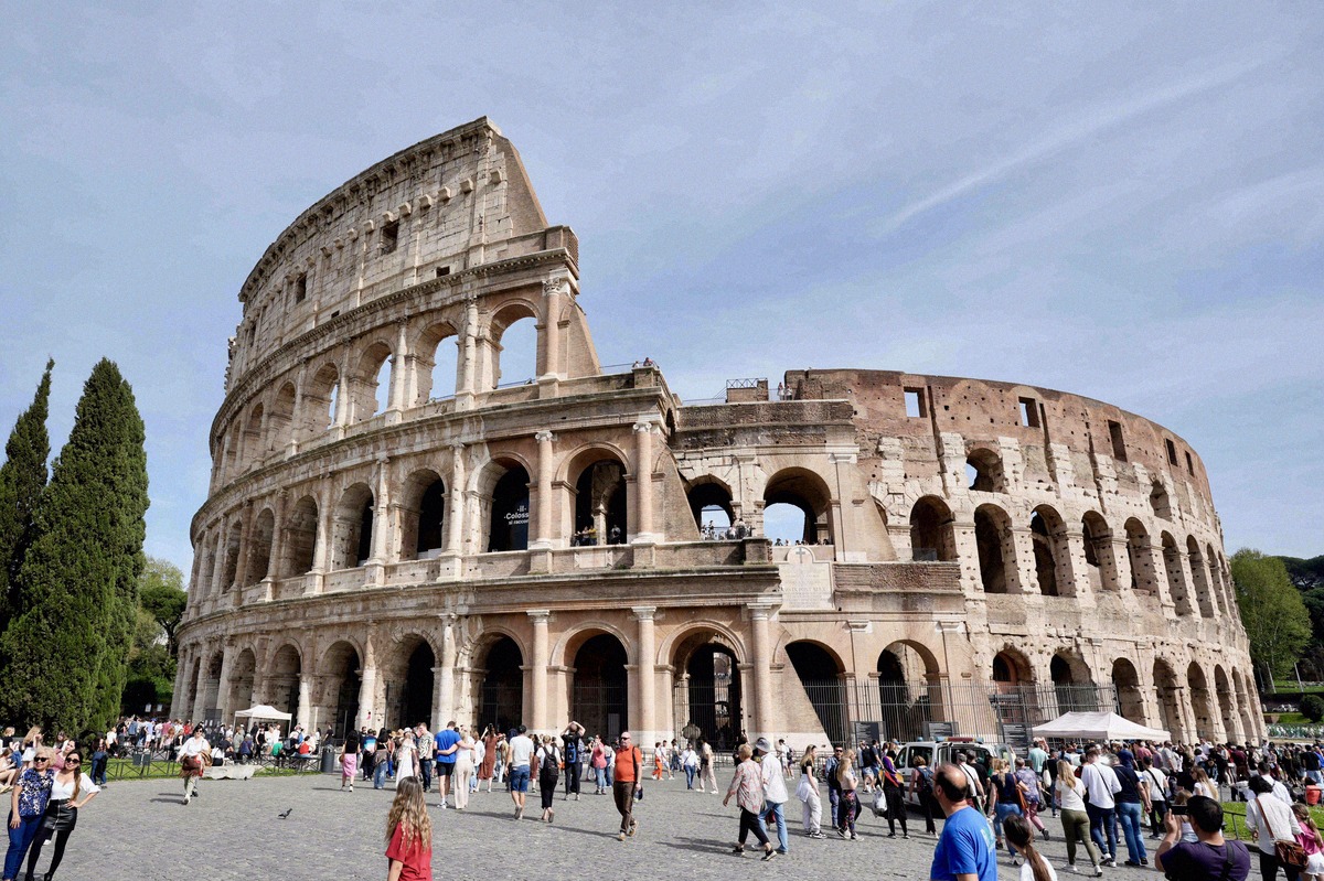 Exterior of the Colosseum with its multi-tiered arcades and visitors on the square in front