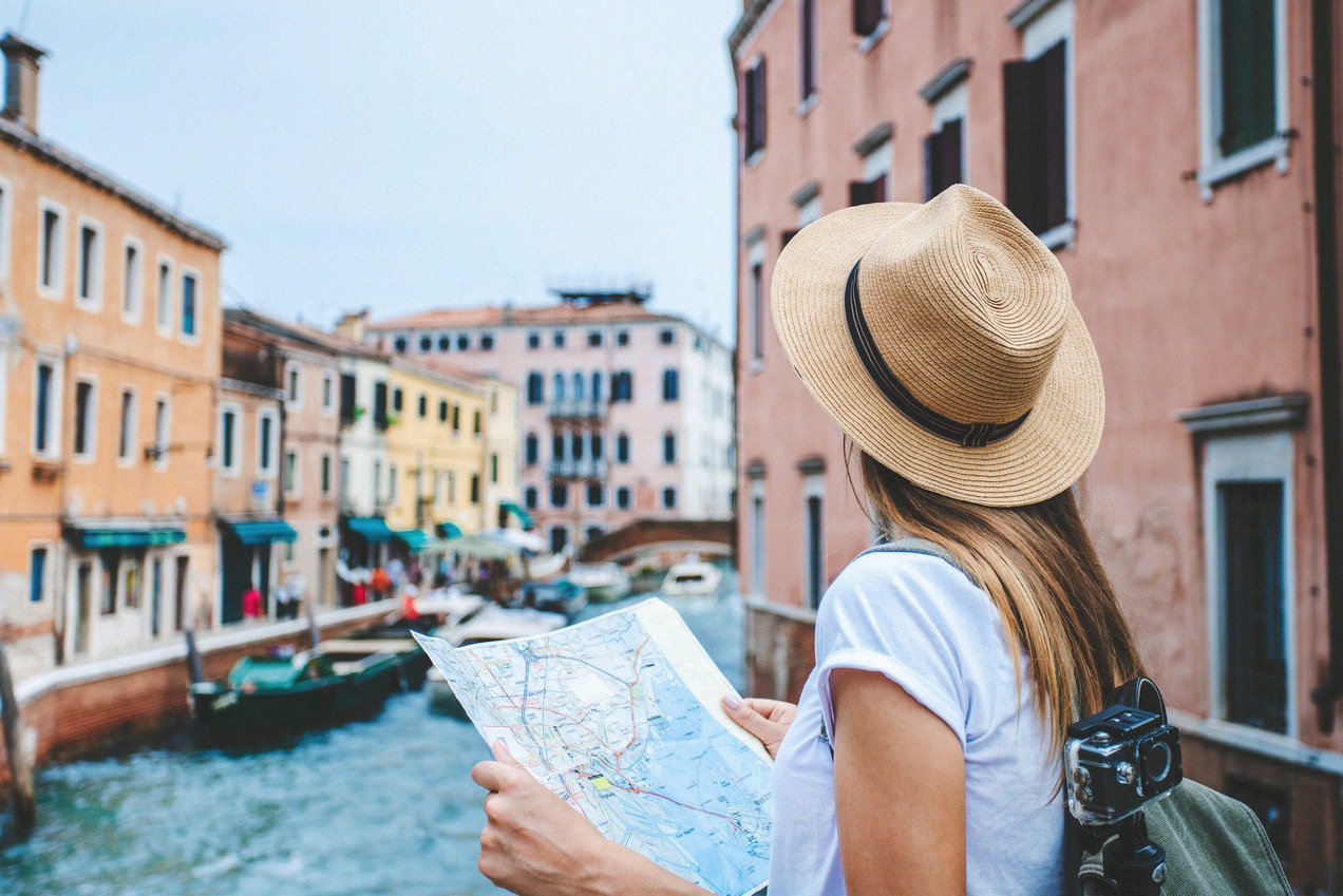 Female tourist on a bridge in Venice overlooking a colorful canal with boats and historic houses