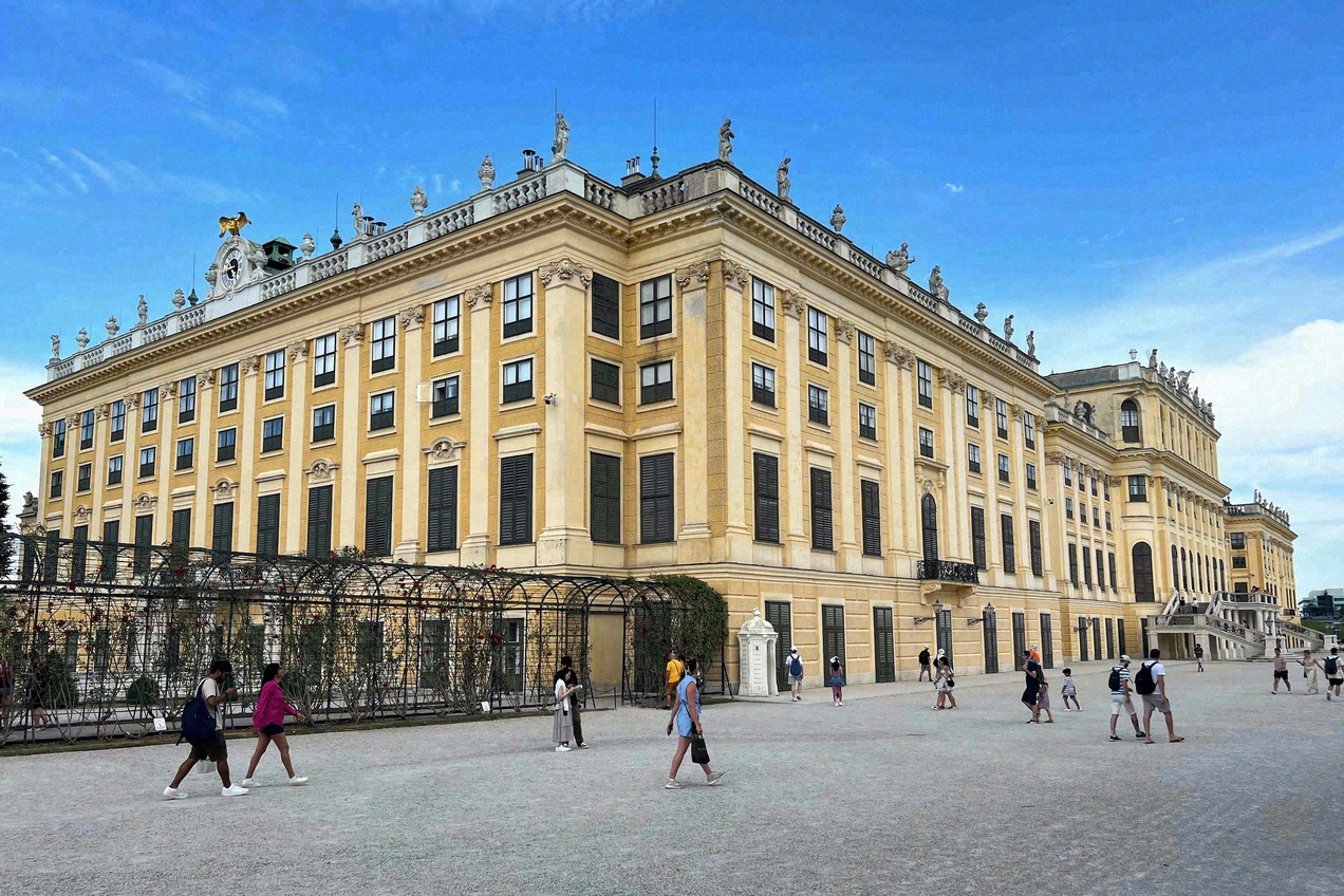 Baroque ochre-yellow main facade of Schönbrunn Palace in Vienna with sculptural decoration and visitors on the forecourt